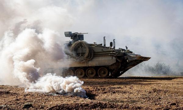 Vehículo blindado de combate avanzando entre cortinas de humo durante unas maniobras militares en terreno abierto